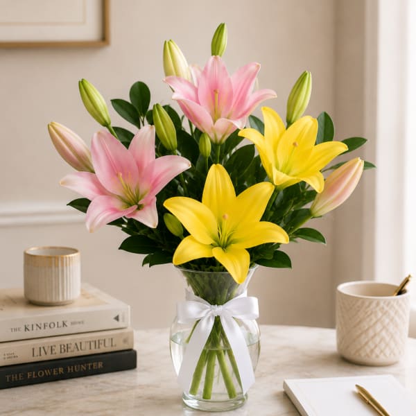 Pink and yellow lilies in a clear glass vase with a white ribbon
