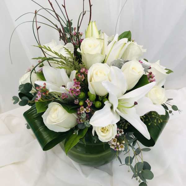 White roses and lilies arranged in a low vase with greenery