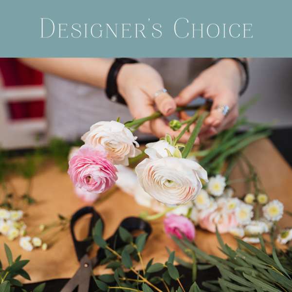 Florist arranging pastel pink and white ranunculus and daisies on a work table