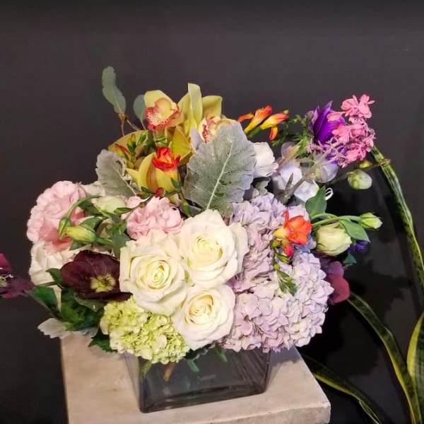 Mixed bouquet of roses, hydrangeas, and orchids in a square glass vase