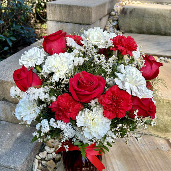 Bouquet of red roses and white and red carnations in a dark vase