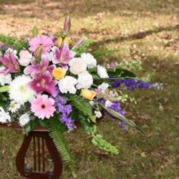 Large mixed flower arrangement with pink lilies, roses, and daisies on a stand