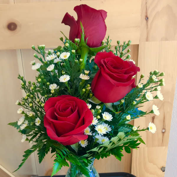 Three red roses with small white daisies in a glass vase