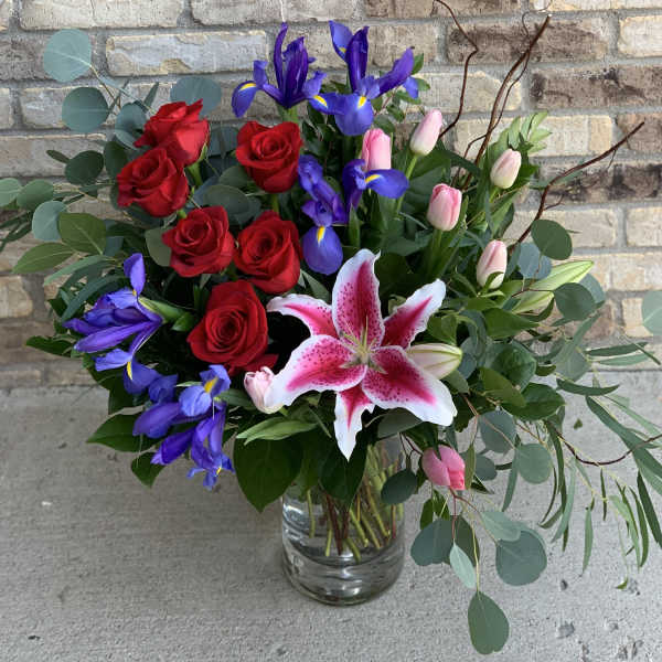 Bouquet of red roses, purple irises, pink tulips, and a pink stargazer lily in a glass vase