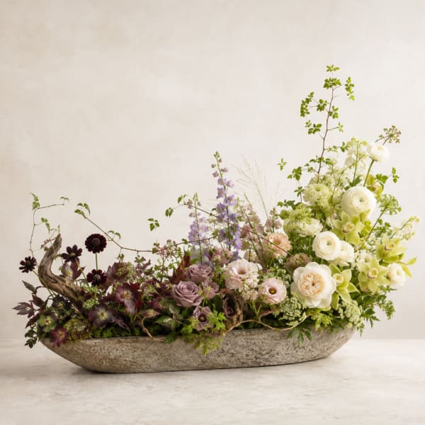 Low floral centerpiece in a stone bowl with white, lavender, and burgundy blooms