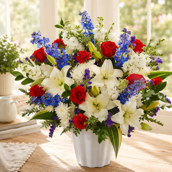 Mixed bouquet of red roses, white lilies, and blue flowers in a white vase