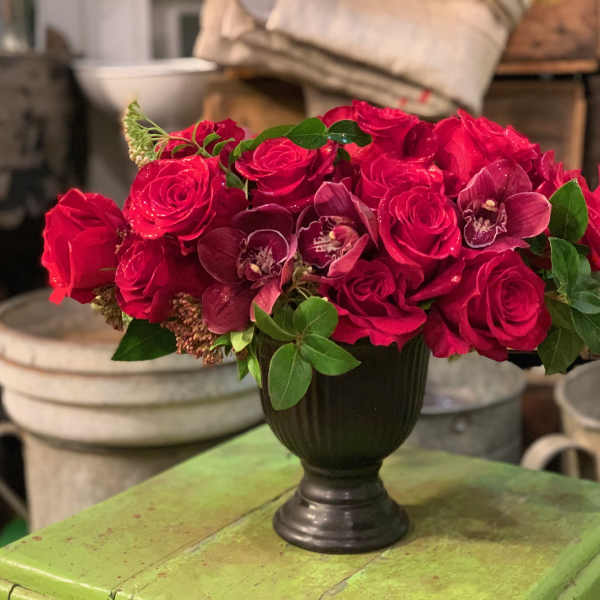 Red rose arrangement with orchids in a dark vase