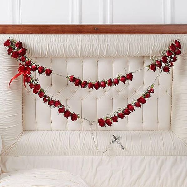 Red rose garlands draped across a white upholstered headboard with a small cross pendant