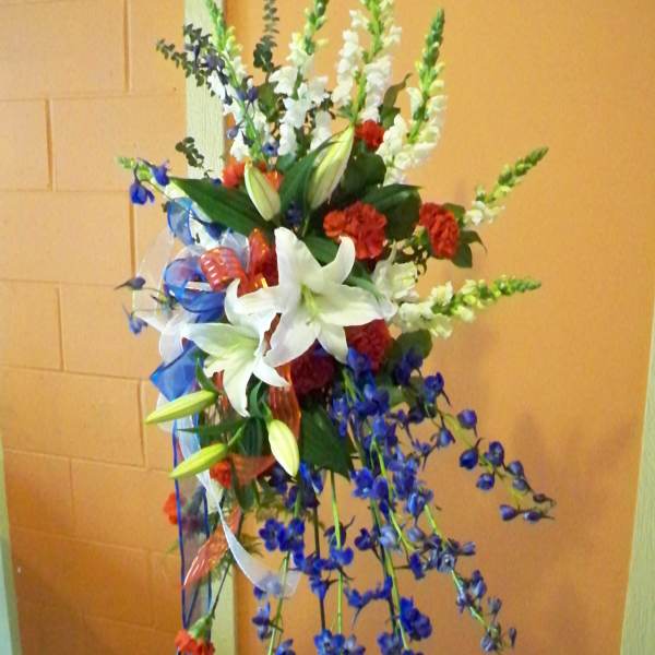 Tall standing floral spray with white lilies, red carnations, and blue flowers