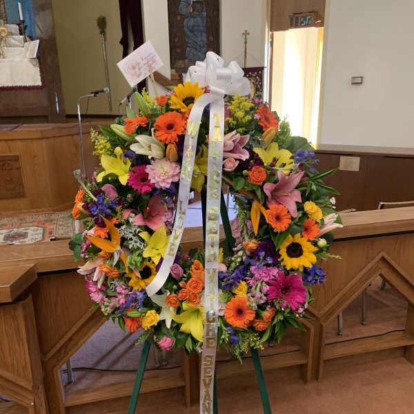Large colorful funeral wreath on an easel with white ribbons