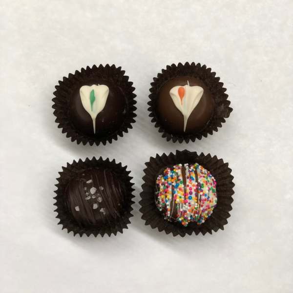Four decorated chocolate truffles in dark paper cups on a white background
