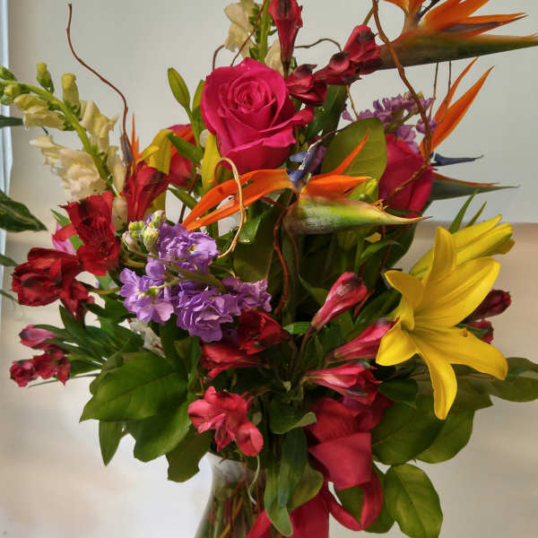 Mixed bouquet with roses, lilies, and bird-of-paradise in a glass vase