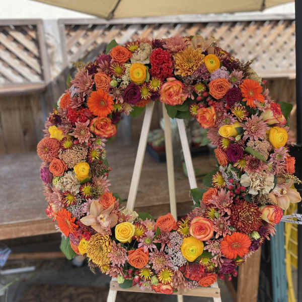 Circular floral wreath on an easel with orange, pink, yellow, and purple blooms