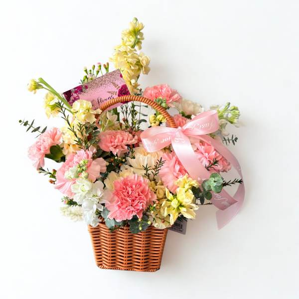 Pink and yellow flowers arranged in a wicker basket with a ribbon
