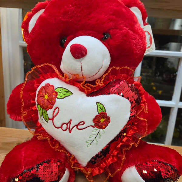 Red teddy bear holding a white heart with the word love