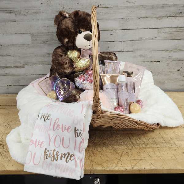Gift basket with a teddy bear, chocolates, and beauty items on a white blanket