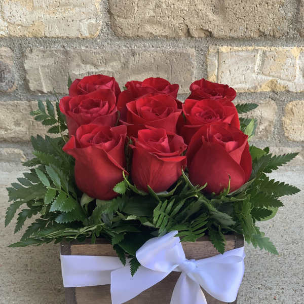Red roses arranged in a wooden box with a white ribbon