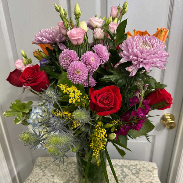 Mixed bouquet of red roses, pink blooms, and lavender flowers in a glass vase