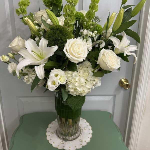 White lilies, roses, and green blooms arranged in a clear glass vase.