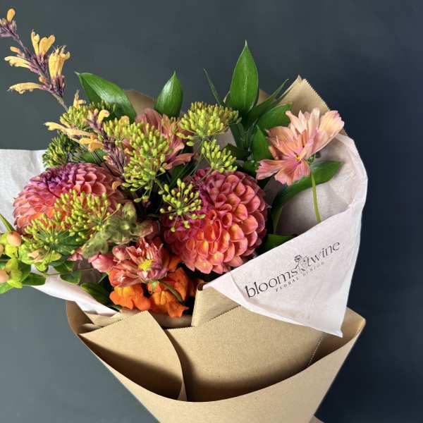 Hand-tied bouquet of pink and orange flowers wrapped in brown paper