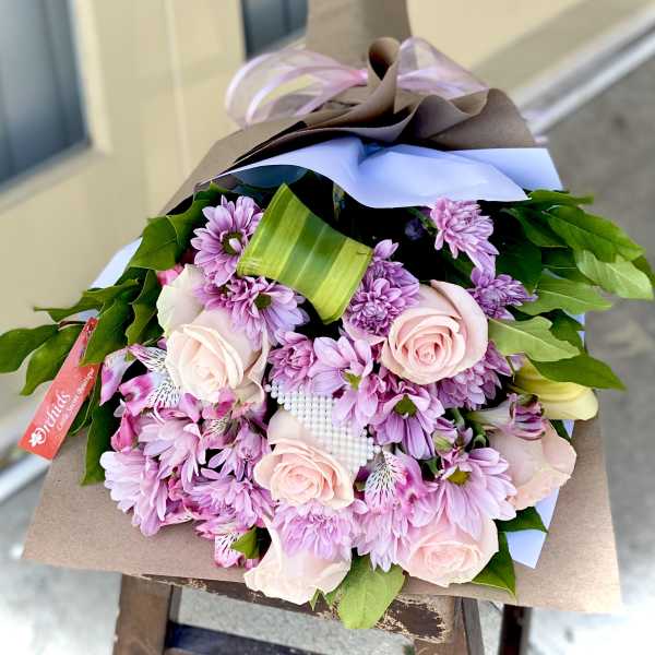 Bouquet of pink roses and purple daisies wrapped in brown paper