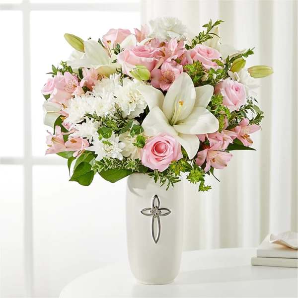 Pink and white flower arrangement in a white vase with a silver cross