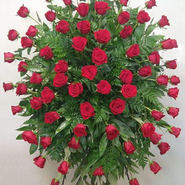 Standing spray of red roses with greenery on a black easel