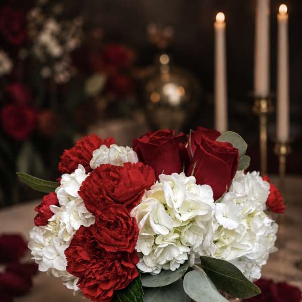 Red roses and white carnations in a glass vase with candles