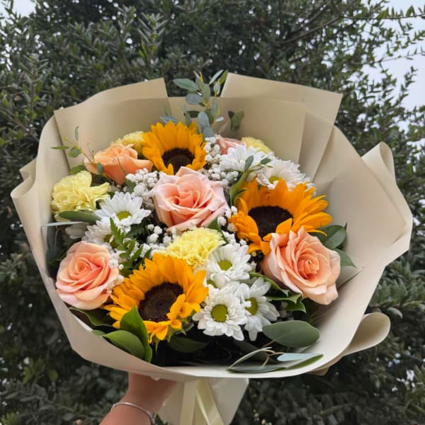 Bouquet of sunflowers, peach roses, and white daisies wrapped in beige paper