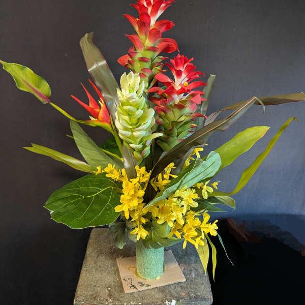 Tropical arrangement with red and green blooms in a teal vase