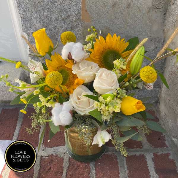 Vase arrangement of yellow sunflowers, white roses, and yellow tulips in a glass cylinder vase
