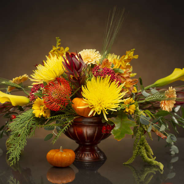 Autumn floral arrangement with yellow blooms in a dark vase and small pumpkins