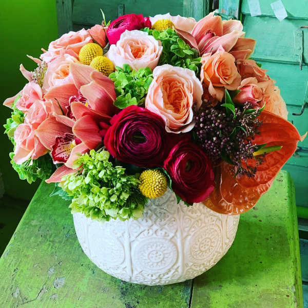 Mixed bouquet of peach, pink, and red flowers in a white ceramic vase