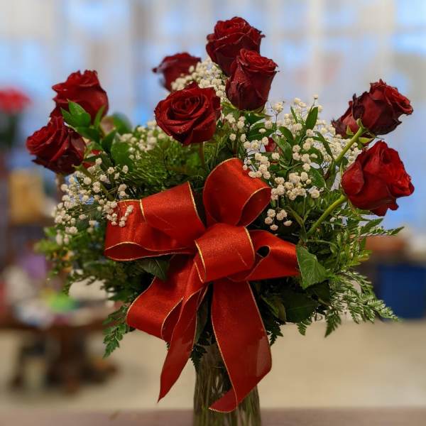 Red roses in a glass vase with baby's breath and a large red ribbon