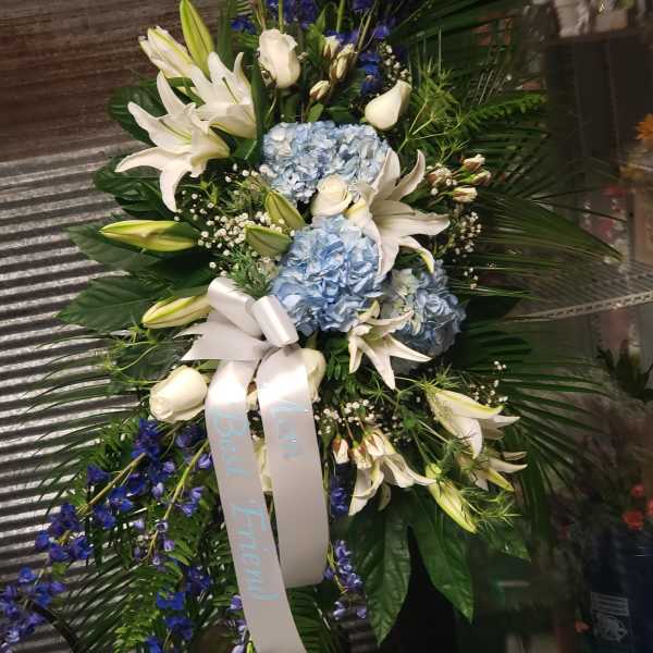 Standing floral spray with white lilies, blue hydrangeas, and blue ribbon
