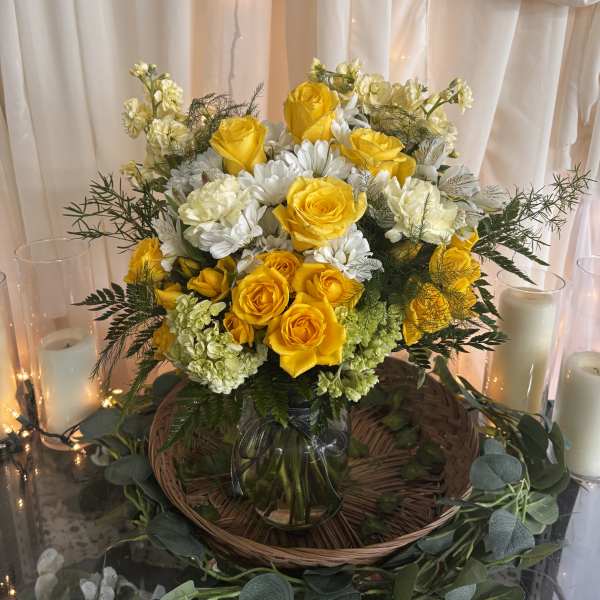 Yellow roses and white flowers in a glass vase with candles