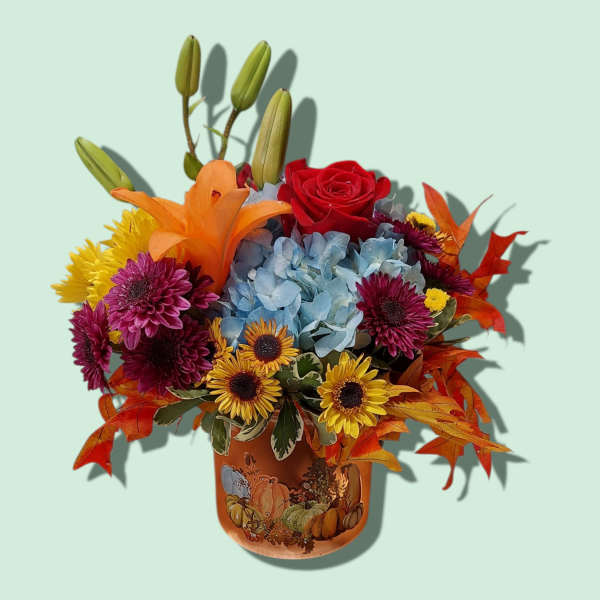Autumn bouquet with red rose, blue hydrangea, lilies, and mums in a pumpkin vase