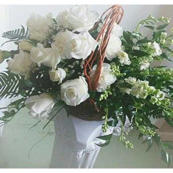 White rose bouquet in a basket-style holder with trailing greenery