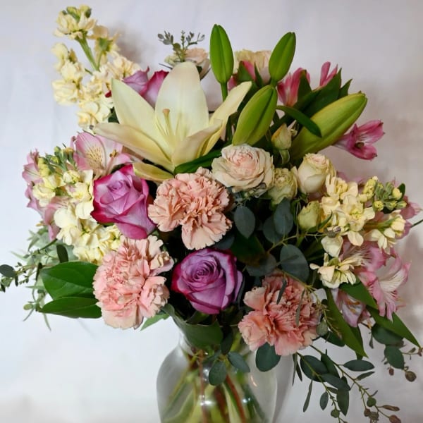 Pastel bouquet of lilies, roses, carnations, and mixed flowers arranged in a clear glass vase