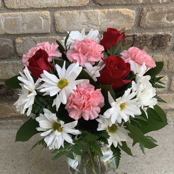 Bouquet of red roses, pink carnations, and white daisies in a glass vase