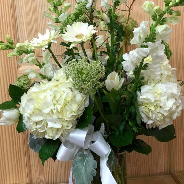 White floral arrangement in a glass vase with a white ribbon