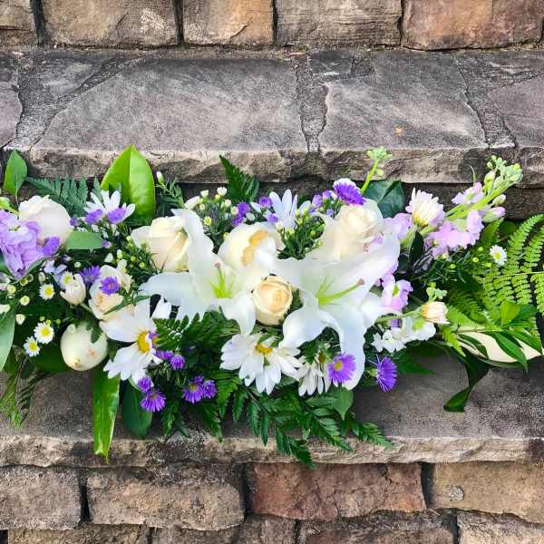 Low white lily and rose arrangement with purple and white daisies and ferns on stone steps