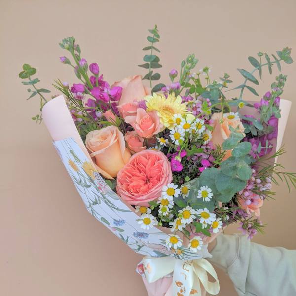 Hand-tied bouquet of peach and pink roses with small white daisies