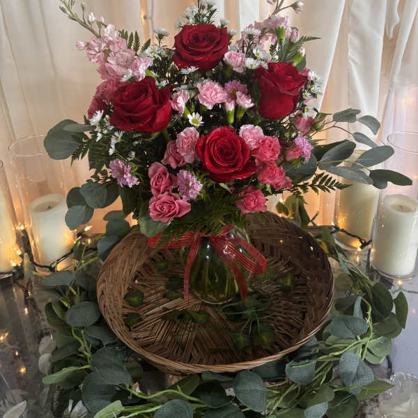Red and pink rose arrangement in a glass vase with candles and draped fabric
