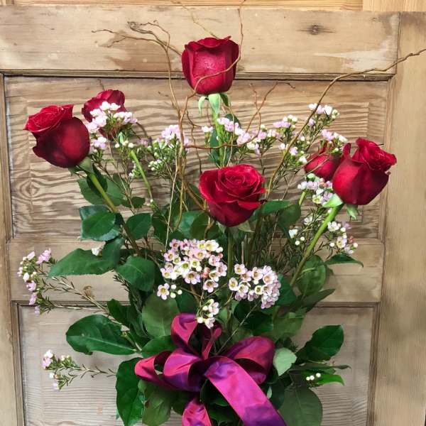 Red roses in a clear glass vase with pink filler flowers and a purple ribbon