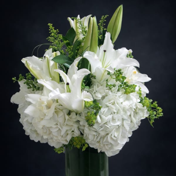 White lilies and hydrangeas arranged in a clear glass vase