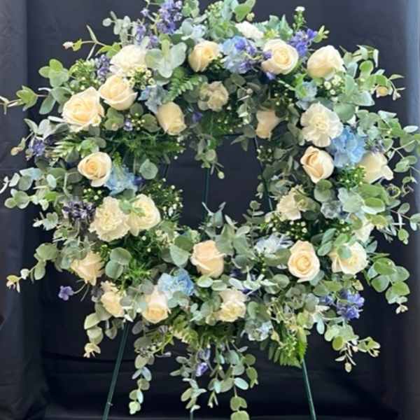 Circular floral wreath with cream roses and blue flowers on an easel