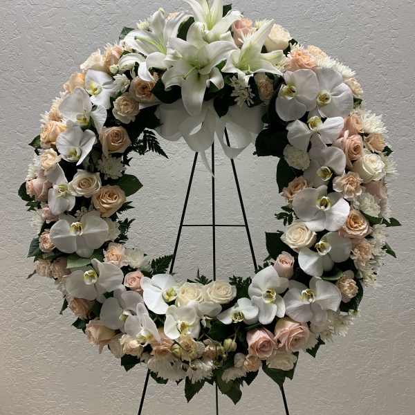 Large floral wreath with white orchids, lilies, and pale roses on a stand