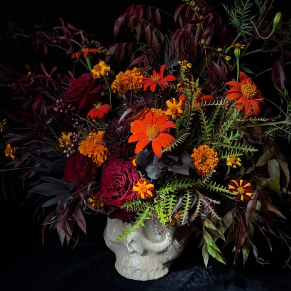 Bouquet of orange and burgundy flowers in a white skull vase