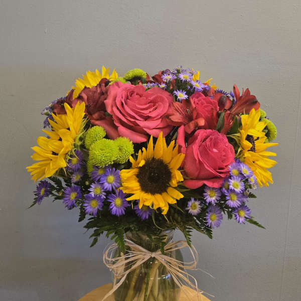 Bouquet of pink roses, sunflowers, and purple daisies in a glass vase